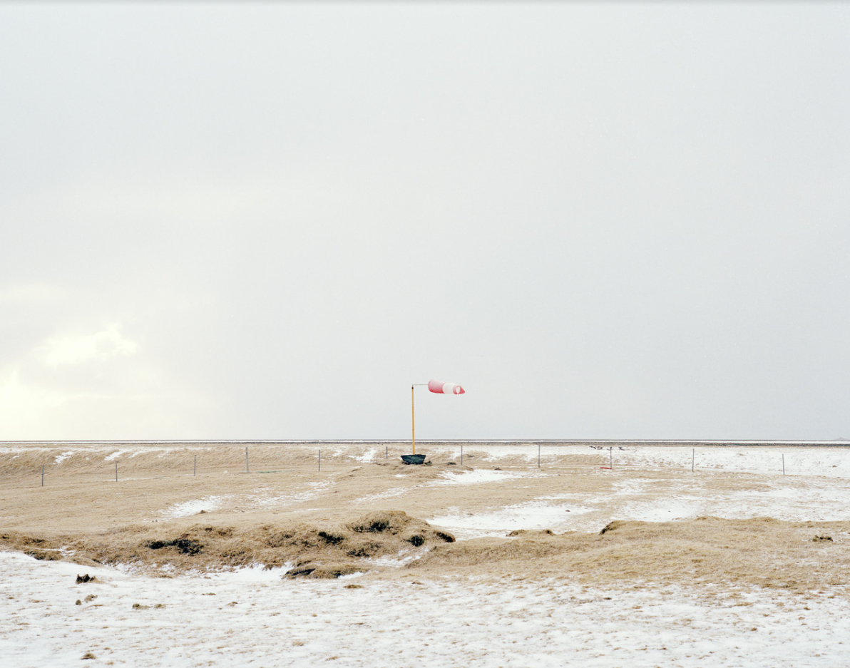 Piaszczysty krajobraz z wodą i małą konstrukcją z flagą w oddali.