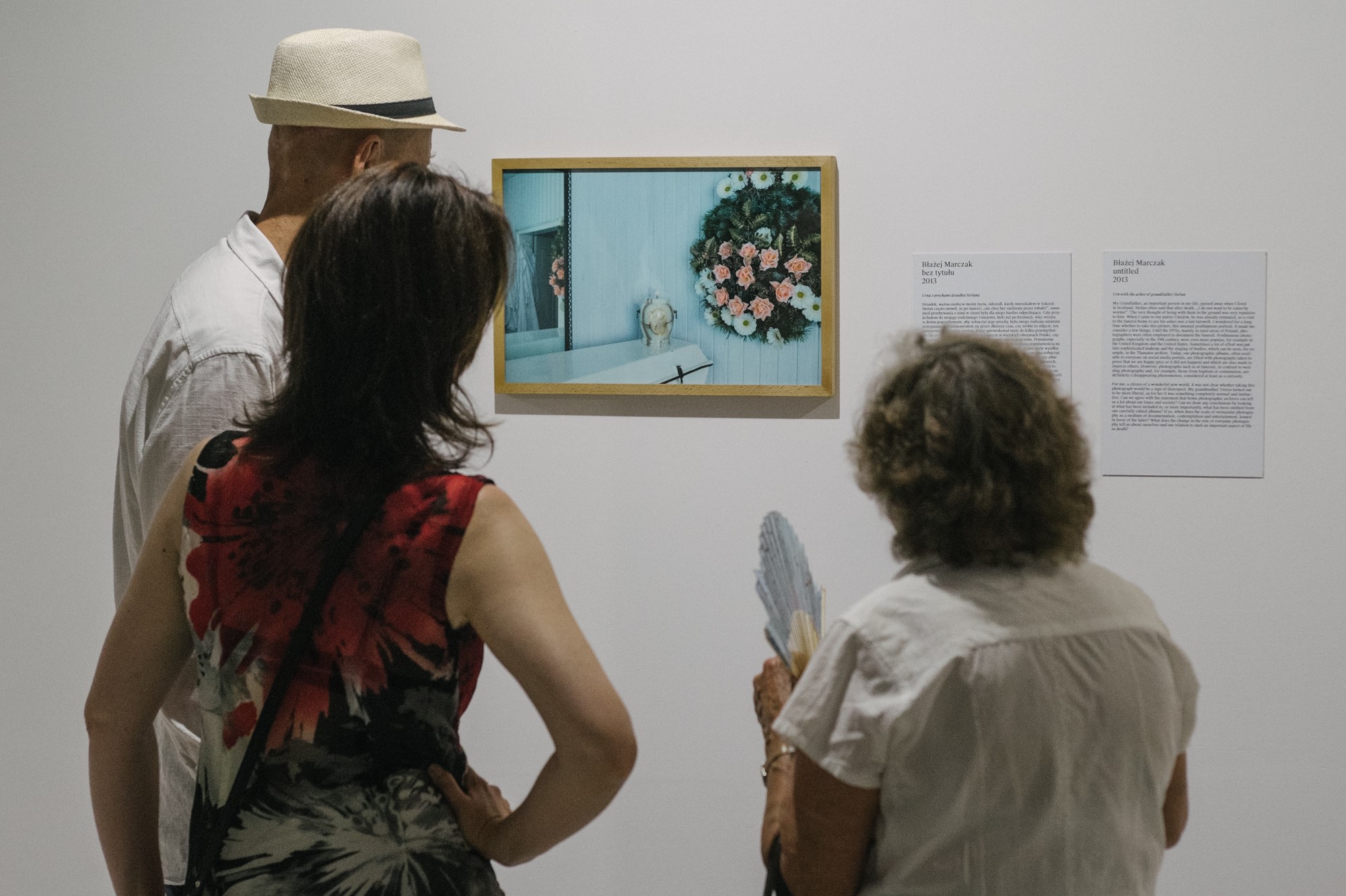 Trzy osoby oglądają oprawioną fotografię na ścianie.