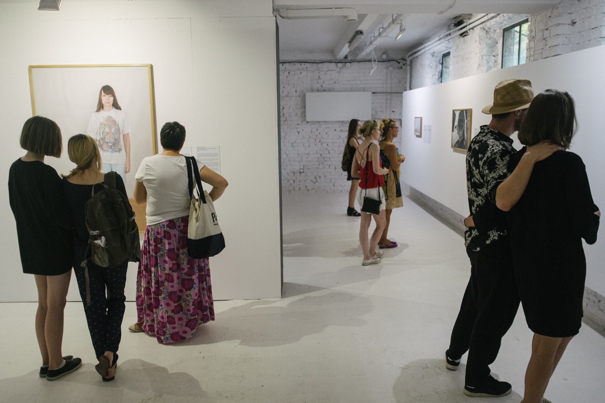 Osoby przemieszczają się w przestrzeni galerii między ścianami ekspozycyjnymi.