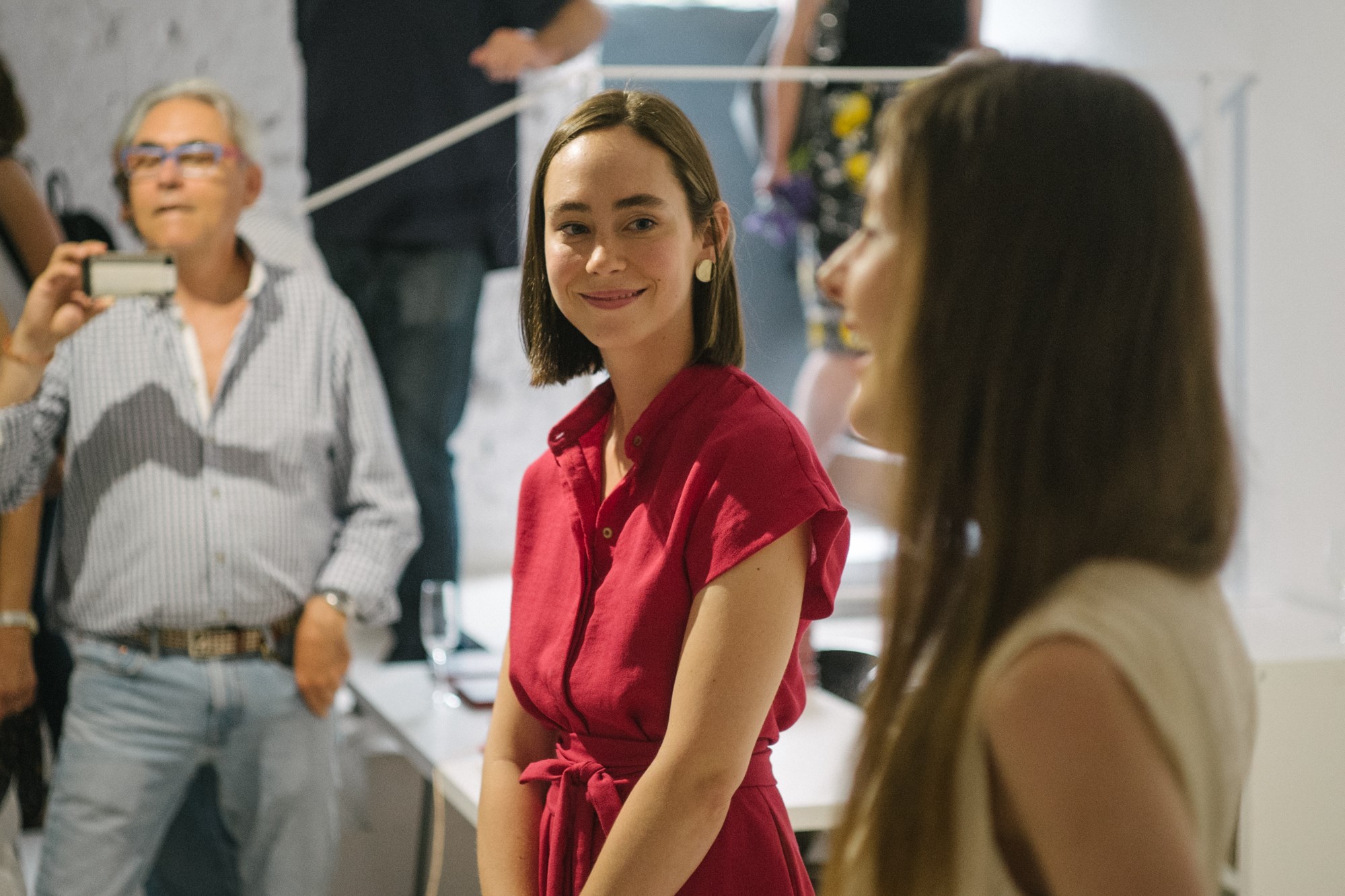 Kobieta w czerwonej sukience stoi w galerii, inne osoby w tle.