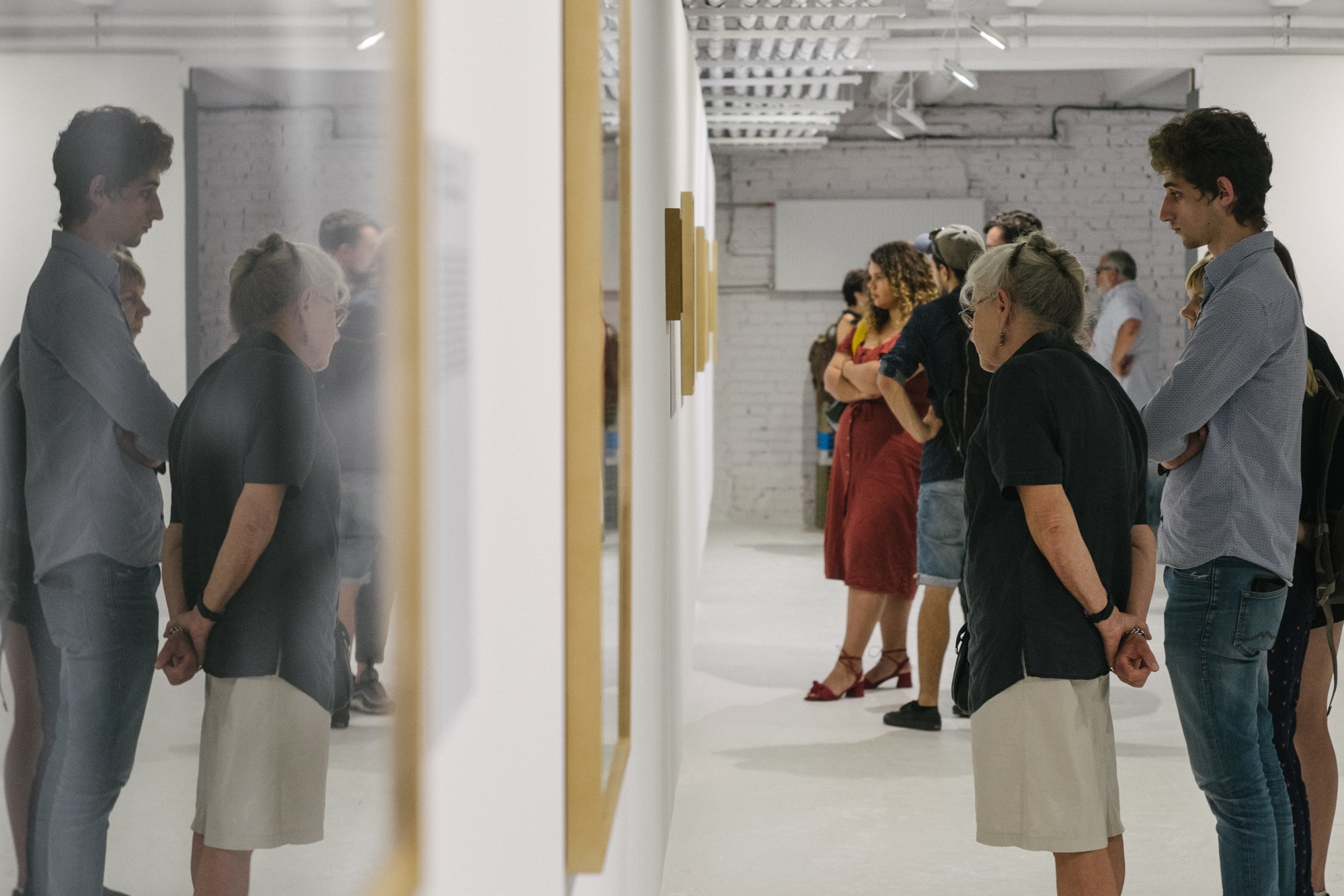 Grupa osób stoi w galerii, oglądając prace na ścianach.